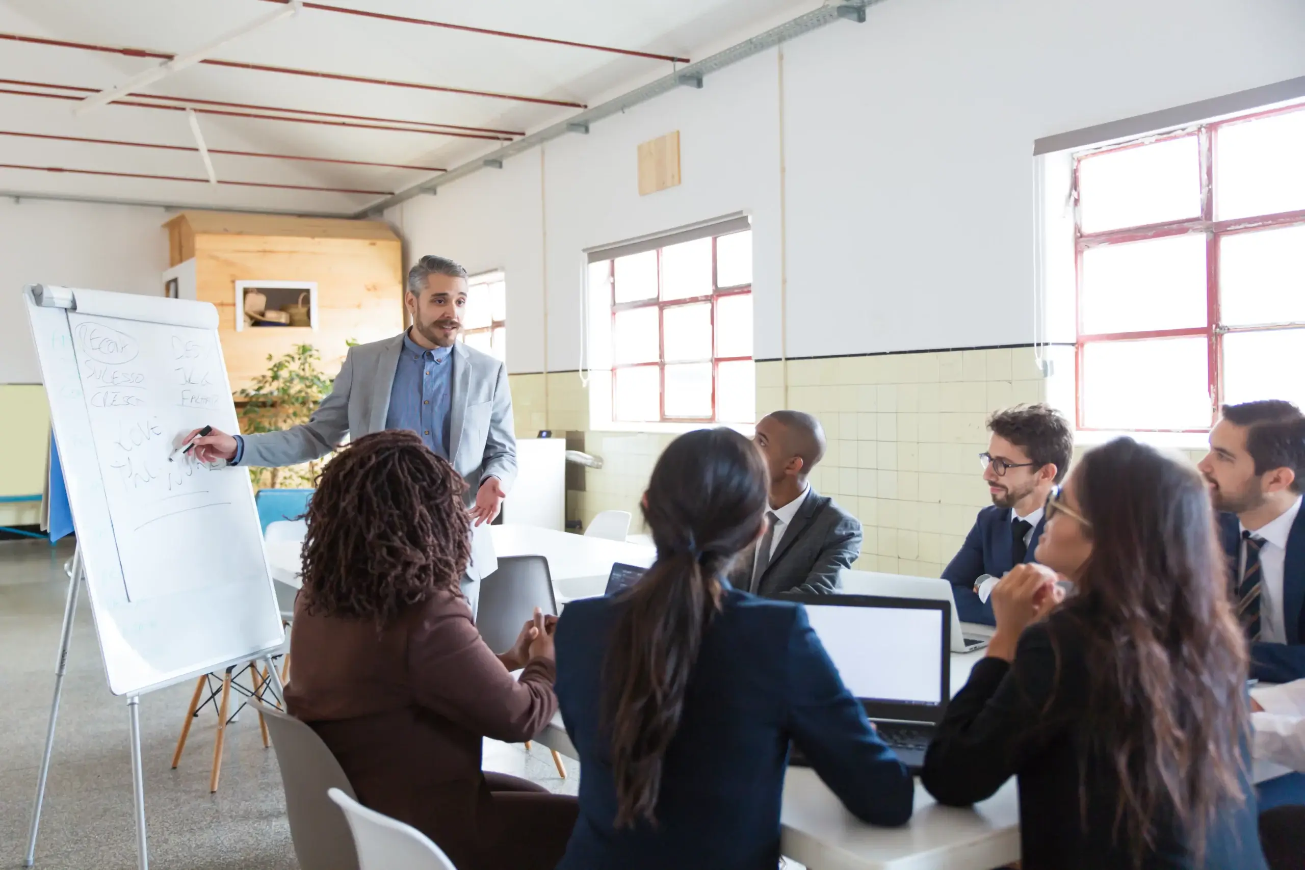 Un formateur expérimenté présente un atelier dynamique dans le cadre de formations pour entreprises. Les participants, attentifs et engagés, prennent des notes et interagissent, soulignant le rôle essentiel des formateurs pour transmettre des savoirs et renforcer les compétences des équipes.